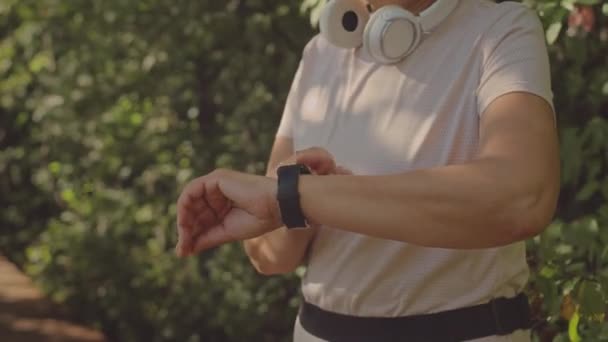 夏に公園で屋外でジョギングしながらスマートウォッチを使用してアクティブなアジアの女性のティルトアップショット — ストック動画