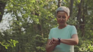 Aktif Asya 'lı bir kadının belden yukarı portresi. Kameraya gülümsüyor. Güneşli yeşil parkta koşuyor.