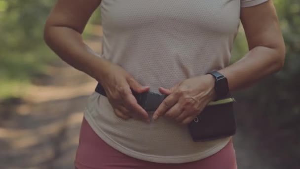パークジョギングのトレイルに立っている間 彼女のスマートフォンを使用して認識できない女性のミス — ストック動画