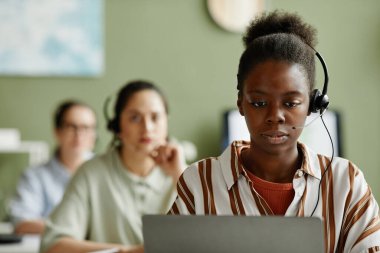 Kulaklık takan Afrikalı genç bir ajan dizüstü bilgisayar başında müşteri hizmetleri destek şirketinde çalışıyor.