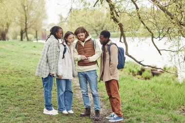 Parkta yürüyüş yaparken yolu bulmak için dijital tablet kullanan çok ırklı bir grup genç.