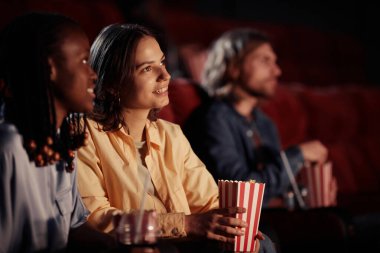 Genç gülümseyen kız sinemada arkadaşıyla film izlerken patlamış mısır yiyor.