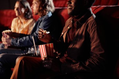 Afrikalı genç adam patlamış mısır yiyor ve arkadaşlarıyla sinemada film izliyor.