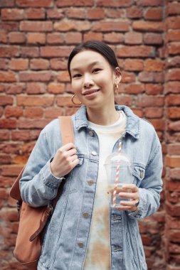 Sırt çantalı ve gazozlu genç ve güzel bir kadın, tuğla bina duvarına yaslanırken el ele tutuşuyor.