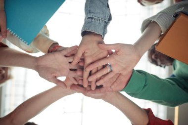 Takım çalışmasının, desteğin, arkadaşlığın ve birliğin sembolü olarak günlük giyimde bir grup genç öğrencinin el altında.