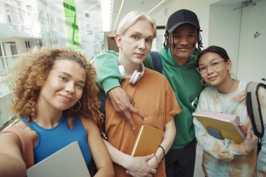 İki kültürler arası mutlu genç çift tatilde ya da dersten sonra üniversite koridorunda selfie çekerken kameraya bakıyor.