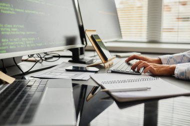 Ofisteki bilgisayar monitörlerinin önünde otururken akıllı telefondan klavyeye kod yazan kadın programcının yakın plan görüntüsü
