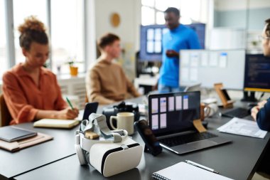 Programcılar yeni yazılımı arkaplanda test ederken VR gözlüklerinin yatay görüntüsü masada yatıyor