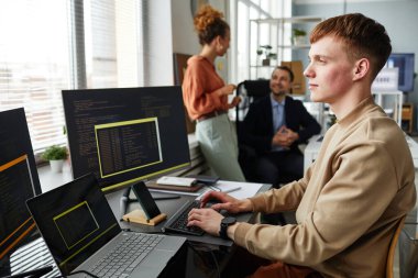 Klavyede yazan ve masada çalışan bilgisayar monitörüne bakan genç programcı, yeni yazılım için kodlar yazıyor