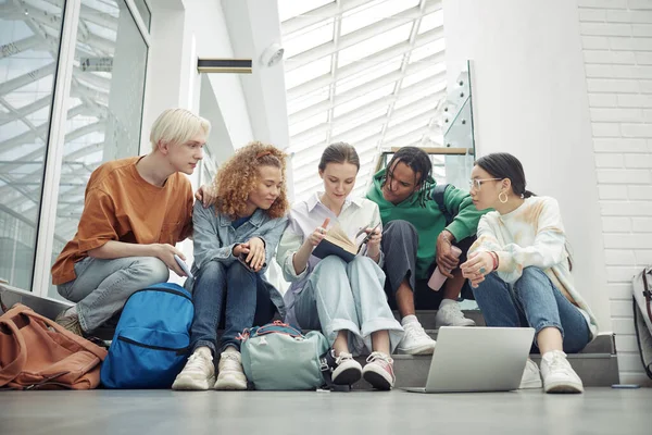 stock image Clever teenage students of college or highschool looking through paragraph in textbook held by one of girls before lesson