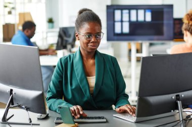 Gözlüklü Afrikalı genç bir kadın ofisindeki bilgisayarında yazılımla çalışıyor.