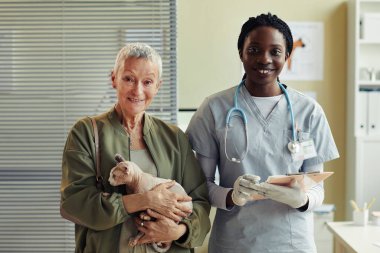 Veteriner kliniğinde poz verirken ve kameraya gülümserken yaşlı bir kadınla genç bayan veteriner portresi.