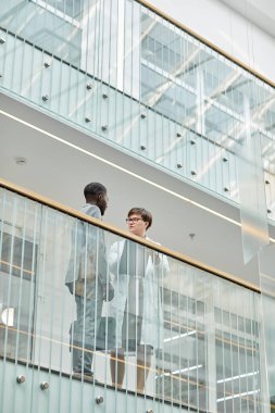 Modern ofis binasının balkonunda cam elementlerle duran iki iş adamının grafiksel düşük açılı portresi.