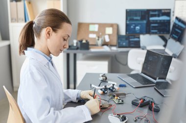 Kalite kontrol istasyonunda donanım parçalarını kontrol eden kadın laboratuvar teknisyeninin yan görünüm portresi, boşluğu kopyala