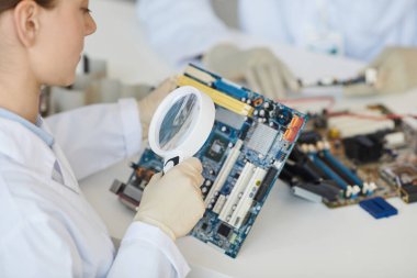 Kadın laboratuvar teknisyeninin kalite kontrolde büyüteçle elektronik parçaları incelemesini kapat, boşluğu kopyala