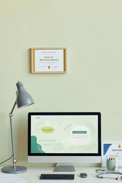 Vertical background image of workplace with computer and certificates in modern vet clinic in green tones, copy space