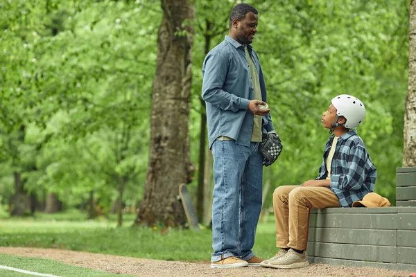 African dad talking to his son before training in baseball in the park