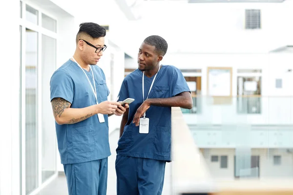 两名身穿制服的多民族医生站在现代诊所大厅聊天 复制空间的肖像 — 图库照片