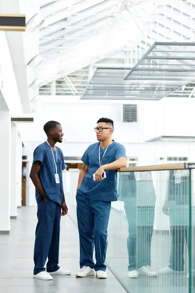 Modern Kliniğin Koridorunda Dikilen Sohbet Eden Üniformalı Iki Çok Irklı — Stok fotoğraf