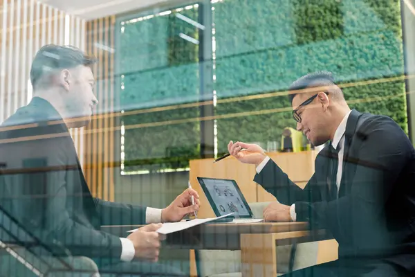 ガラスの壁の後ろの会議室の会議室の会議の間にスーツを身に着けている2人の成功したビジネスの低い角度の肖像画 — ストック写真