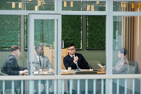 グラスウォールの後ろの会議室で会うビジネスマンのグラフィックショットは 同僚に耳を傾けるハンサムなアジアのビジネスマンに焦点を当てます — ストック写真