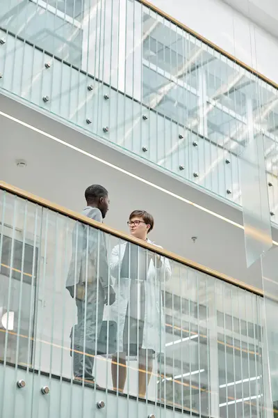 Graphic low angle portrait of two business people standing at balcony in modern office building with glass elements