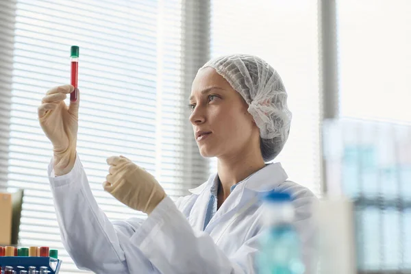 Portrait of female lab technician inspecting test tube with red liquid, copy space