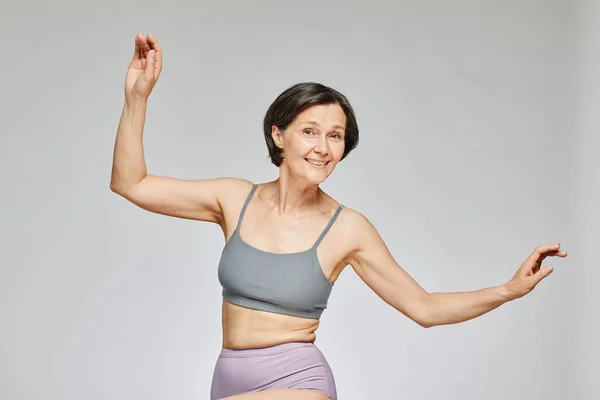 stock image Minimal waist up portrait of carefree mature woman wearing neutral underwear dancing against grey background, body positivity concept, copy space