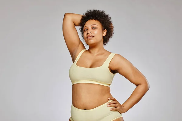 Minimal waist up portrait of confident black woman wearing neutral underwear against grey background, body positivity concept, copy space
