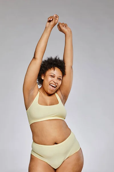 stock image Vertical portrait of carefree black woman wearing underwear and posing happily against grey background
