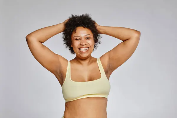 Minimal waist up portrait of carefree black woman wearing underwear and laughing happily against grey background