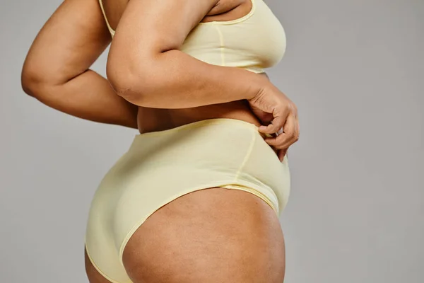 Minimal closeup of unrecognizable black woman wearing underwear against grey background, focus on hips and cellulite, body positivity