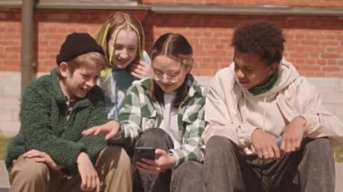 Çok kültürlü bir grup genç arkadaş yazın dışarıda takılırken akıllı telefondan oyun oynuyorlar.