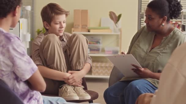 他の子供とグループセラピーセッションをしている間 アフリカ系アメリカ人女性心理学者と話すコーカサス州の十代の少年たちのスローモ — ストック動画