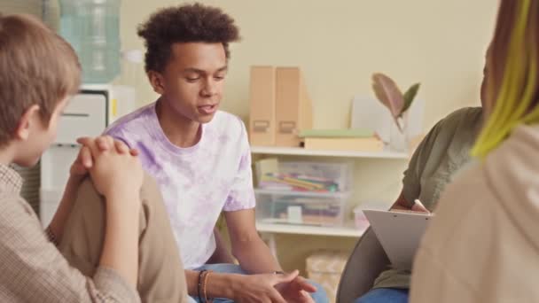 グループセラピーセッション中にアフリカ系アメリカ人女性心理学の専門家と話すBiracial十代の少年の中央スローモ — ストック動画