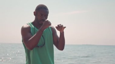 Sahilde tek başına savaşan vahşi siyahi bir adam. Güzel pembe bir gün batımı ve arka planda parlak mavi bir su.