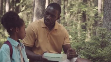Afrika kökenli Amerikalı 8 yaşındaki kız babasıyla yaz günü ormanda öğle yemeği yiyor.