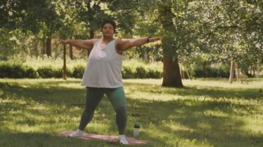 Güneşli bir günde parkta yoga yapan kıvrımlı olgun zenci kadın.
