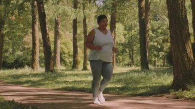 Vücut ağırlığı tam boy pozitif olgun Siyah kadın yaz mevsiminde parkta koşuyor