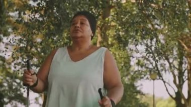 Düşük açılı, kıvrımlı, kararlı siyah kadın spor giyimli, kuzeyli güneşli bir günde parkta yürüyor.