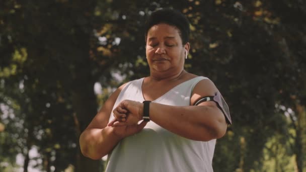 中年非洲裔美国女人夏天在公园里慢跑时 在她聪明的身体上装上定时器的慢动作 — 图库视频影像