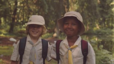 Sırt çantalı ve yeşil yaz ormanlarında kameraya gülümseyen iki izci çocuğun belini kaldırın.