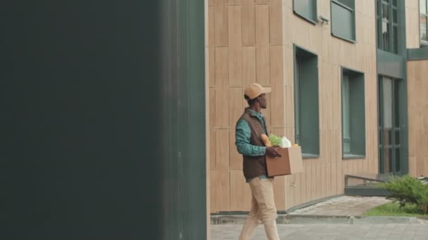 中镜头的年轻黑人杂货送货员走进现代生活区 向顾客提供新鲜食品 — 图库视频影像