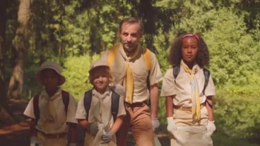 Yaz ormanlarında kameraya poz veren, çevreyi temizlemeye yardım eden çeşitli çocukların olduğu orta boy bir scout portresi.