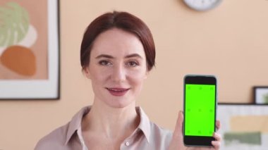 Kafkasyalı genç bir kadının yakın çekim görüntüsü. Şablon ekranla akıllı telefon gösterisi yapıyor ve kameraya konuşuyor.