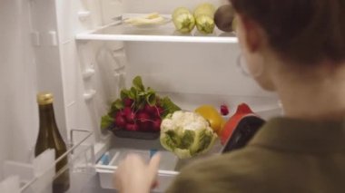 Kafkasyalı genç bir kadının evde yemek pişirirken yiyecek ürünlerini buzdolabına koyması.