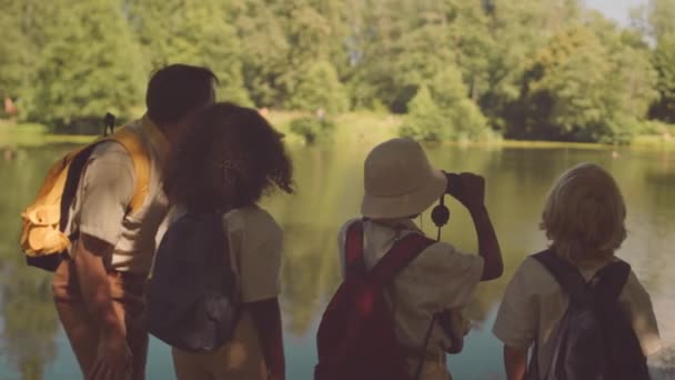 夏に一緒にスカウトしながら 森の川を眺めながら 大人の白人男性教師と多民族の子供たちの背中を見る — ストック動画