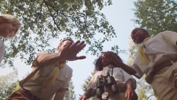大人の白人男性スカウトリーダーとマルチテクニックのスカウトの低角度ショットは 晴れた日の森で屋外に手を置く — ストック動画