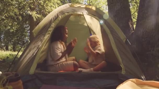 陽気な多民族カップル 小学生のスカウトの友人 森の屋外でテントに座ってハンドクラッピングゲーム — ストック動画