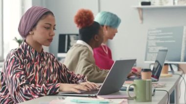 Modern ofisteki dizüstü bilgisayarlarıyla sohbet eden genç ve yaratıcı programcılardan oluşan bir ekip.